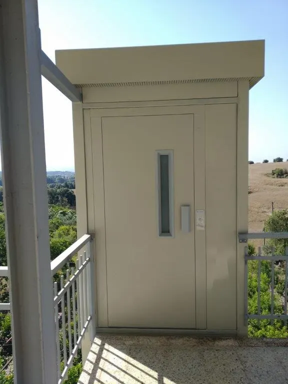 Cream OnLevel EV8 lift with vision-panel door on a terrace overlooking hills