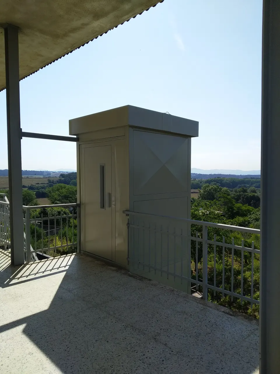 Cream sheet-metal OnLevel EV8 lift shaft on a terrace overlooking open countryside