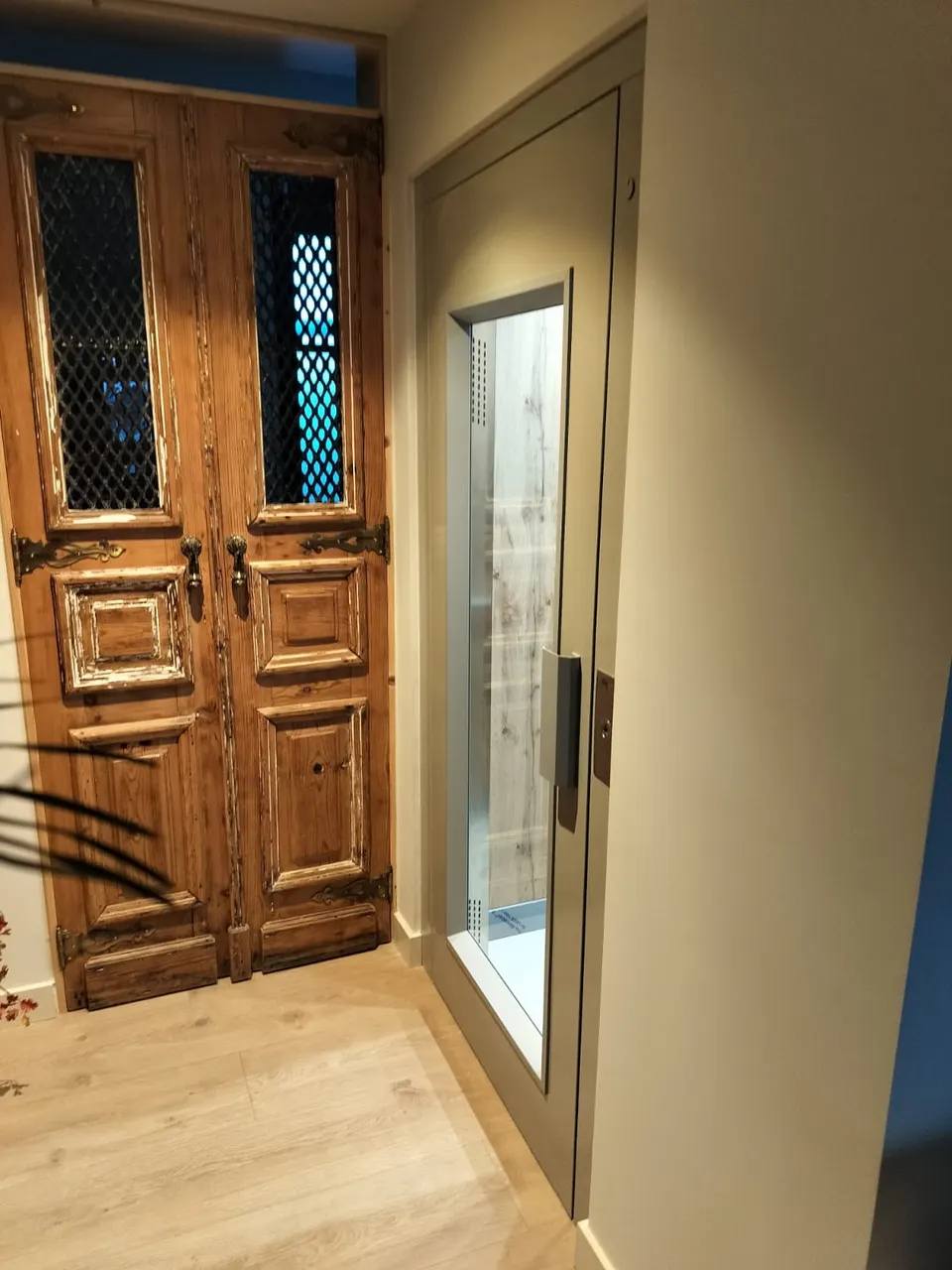 Modern glass OnLevel TV300 home lift installed beside an antique carved timber door