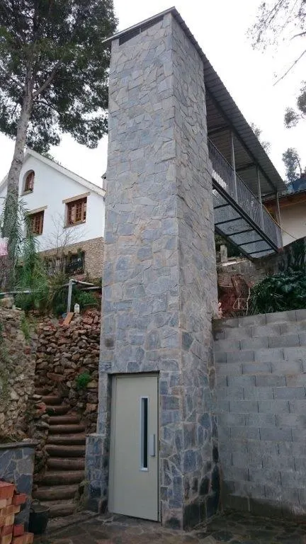 Natural stone-clad OnLevel lift shaft integrated into a hillside home with steel walkway