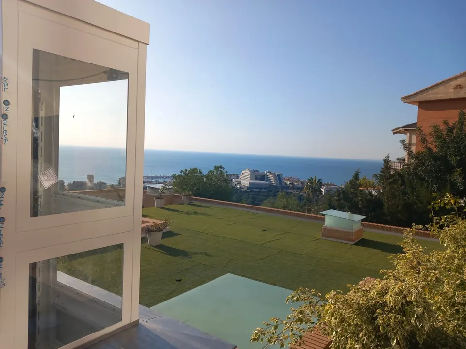 Glass OnLevel TV300 home lift tower on a sunny terrace with sea view